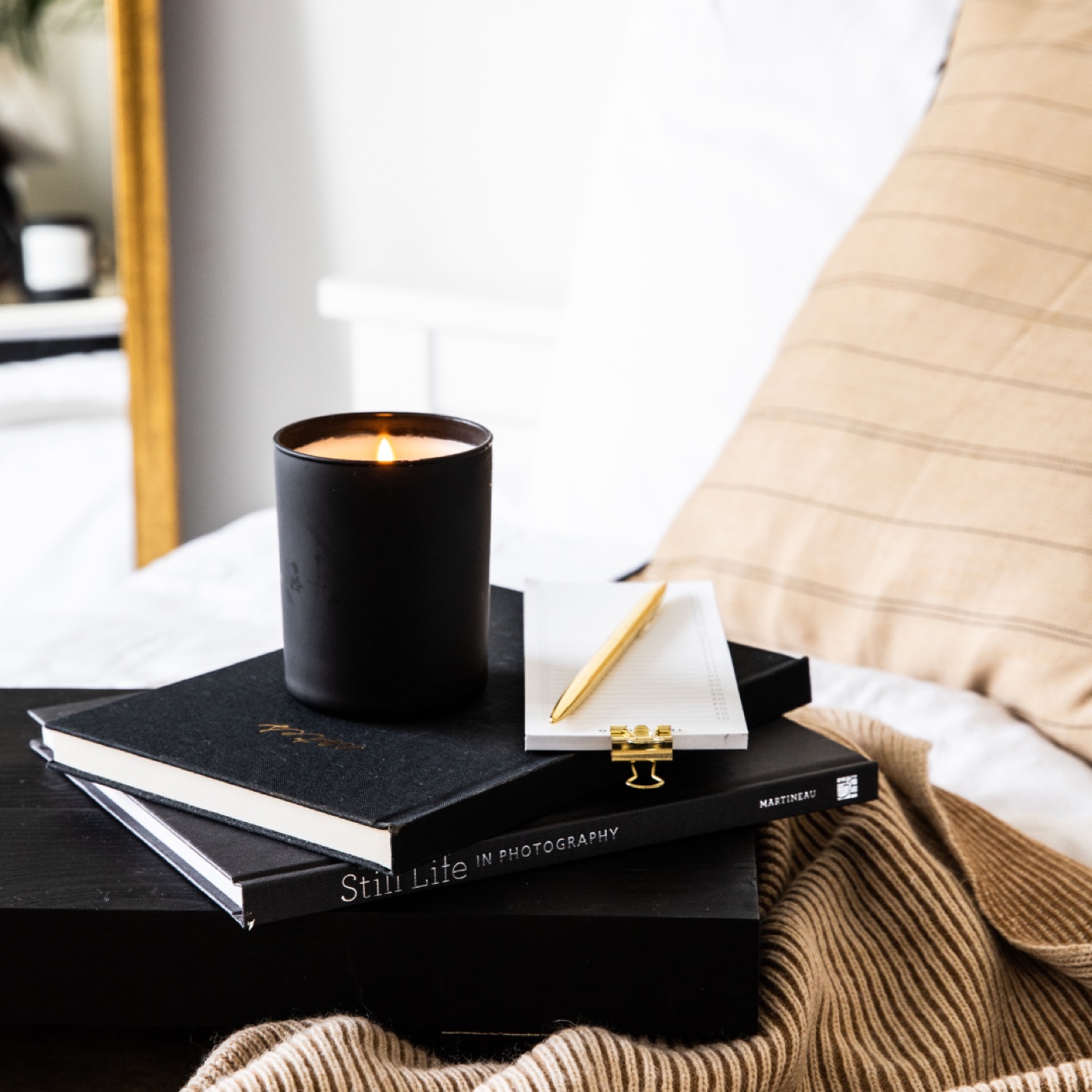 A candle and notebooks styled on a bed